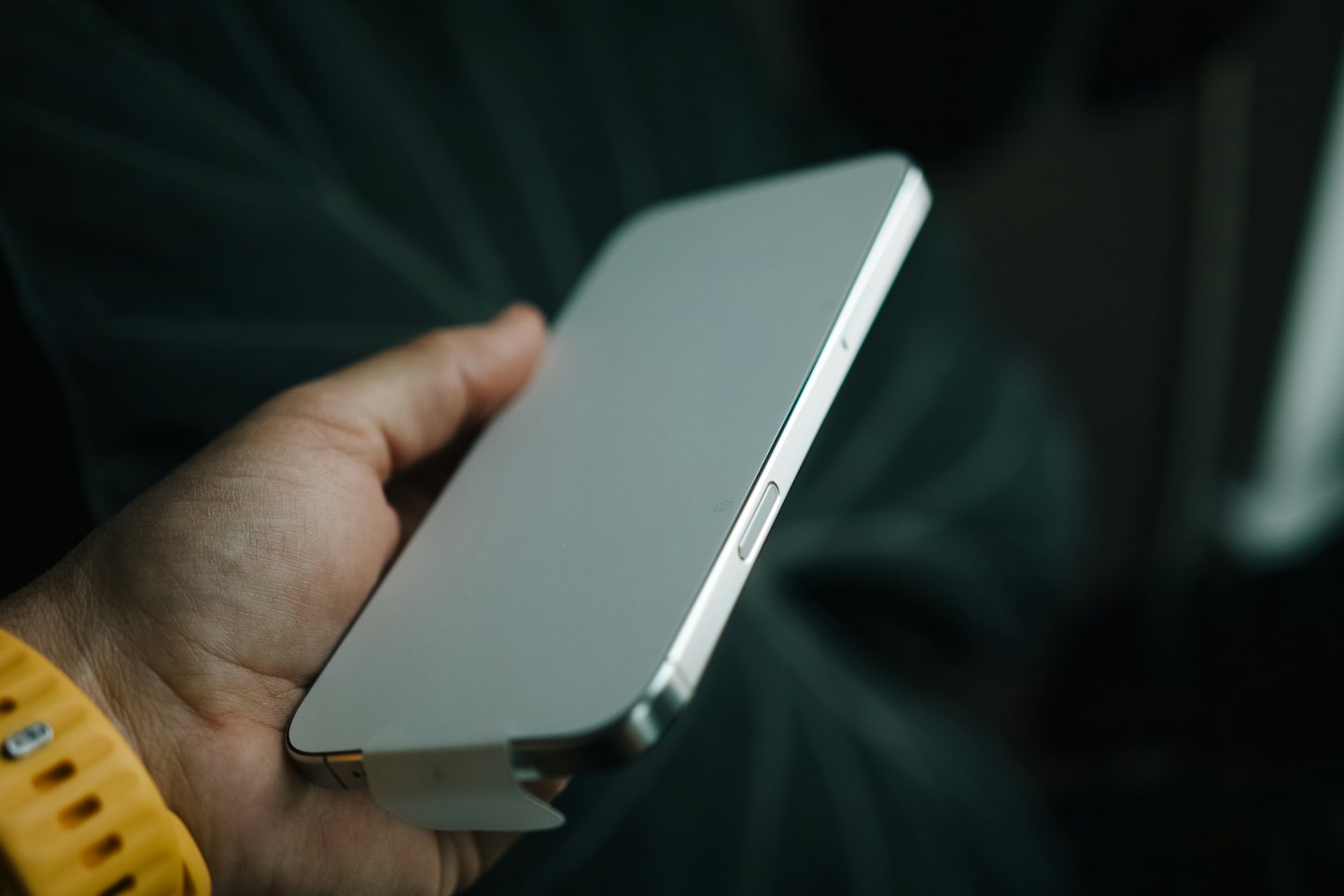 Person's hand holding new smartphone with screen protector peeling.