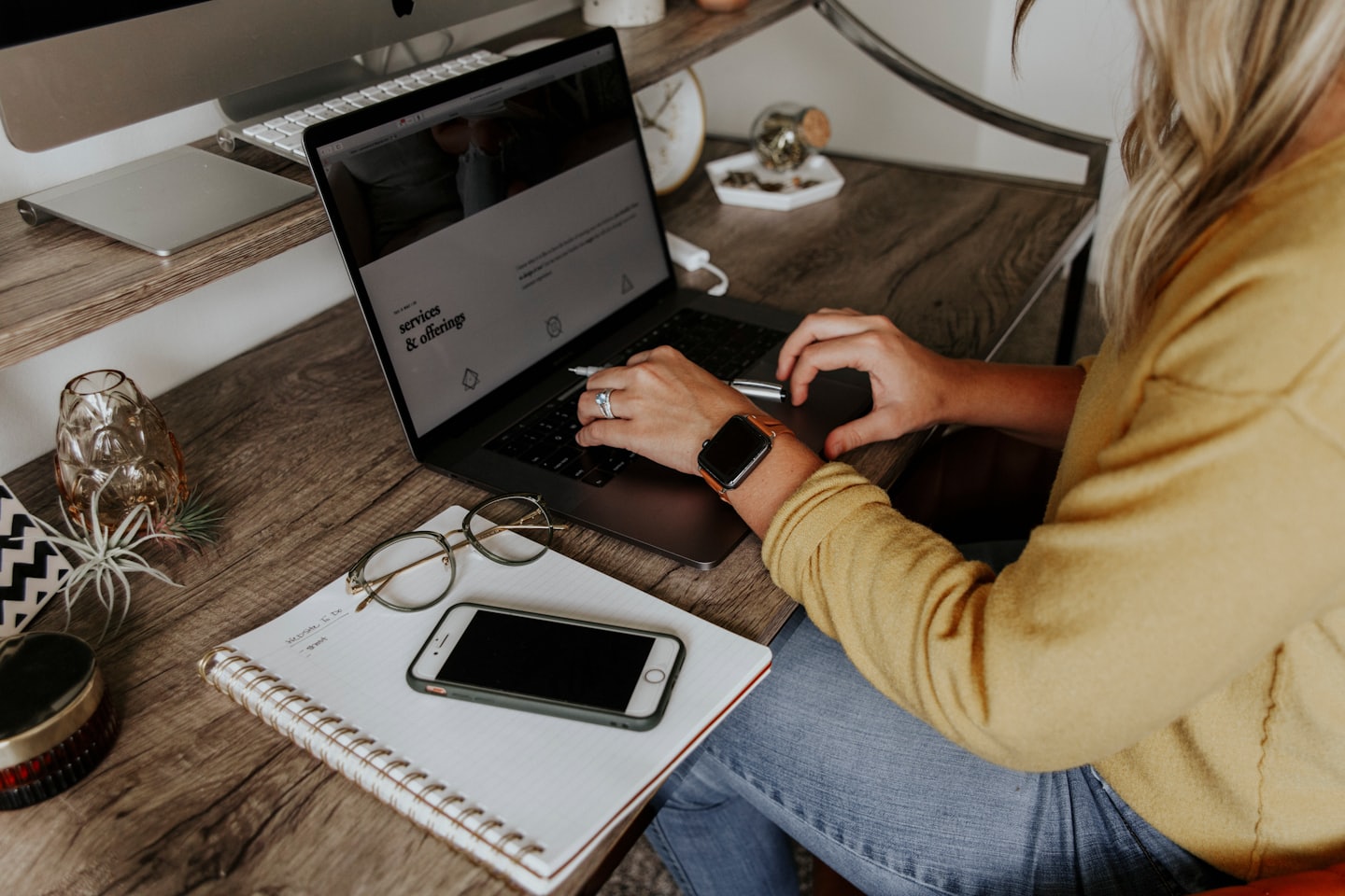 Person in a yellow top working on a laptop at a wooden desk.
